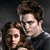 Two people with brown hair pose closely together against a dark background, one person's head resting near the other's shoulder.