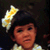 A small image of a child with dark hair wearing a white and yellow flower headband, positioned on the left side of a red background.