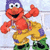 Red muppet character with purple hat, yellow overalls, green boots, and red suspenders in a dancing pose with one arm raised.