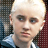 Static pixelated image of a person with light skin, dark eyes, and short white hair wearing a blue shirt against patterned background.