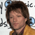 Pixelated image of a person with brown hair wearing a yellow jacket over a dark shirt, with partial text fragments visible around the edges.