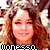 Pixelated static image of a person with long brown hair, closed eyes, and a smiling expression wearing a black-and-white checkered top.