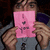 A pixelated image shows a person holding a pink sign with dark symbols against a blurred background.
