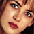 Pixelated close-up of a person's face with brown hair, blue eyes, and red lips on a dark background.
