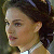 Pixelated close-up of a person's face with dark hair and light skin, wearing a white top against a blurred background.