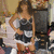 A woman in a black and white strapless dress poses with one hand on her hip against a blurred background.
