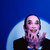 Pixelated image of a person with light skin tone, dark hair, and a black top against a blue background with light gradient.