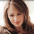A pixelated close-up of a person with light brown hair, closed eyes, and red lips, wearing a dark top against a light background.