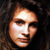 Pixelated close-up of a person's face with light skin tone, dark hair, and neutral expression against dark background.