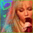 Pixelated image of a person with light brown hair and closed eyes, mouth open in an expressive pose against a multicolored background.