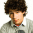 Pixelated image of a person with curly brown hair wearing a light gray collared shirt over a red undershirt, with blue pixelated text surrounding the figure.