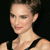 Pixelated close-up of a person with short dark hair, light skin, and a black strap visible on the shoulder against a dark background.