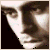 A pixelated close-up of a person's face with dark hair, showing a portion of the forehead, eye, and cheek against a dark background.