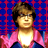 Pixelated static image of a person with brown hair wearing glasses and a pink jacket over a white shirt against a blue-and-red checkered background.