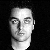Static grayscale pixelated image of a human face with neutral expression, dark hair, and visible neck against black background.