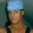 Pixelated image of a person wearing a light blue cap, dark shoulder straps, and a brown torso against a teal background.