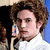 Pixelated close-up of a person with curly brown hair holding a microphone, wearing a white shirt against a blue and beige background.