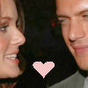 Two people in profile view face each other against a dark background with a pink pixelated heart symbol centered below their faces.