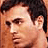 Pixelated static image of a person's face with dark hair and light skin tone, cropped to show upper head and shoulder area against warm-toned background.