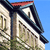 Pixelated image of a house with a red roof, dark trim, and greenery below against a blue sky.