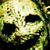 Pixelated static image of a skull with green and yellow tones, dark eye sockets, and visible teeth against a blurred background.