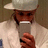 A pixelated figure wearing a light-colored wide-brimmed hat and white shirt, holding an object near the face.