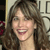 Static 50x50 pixel icon showing a smiling woman with long brown hair against a light background, partially obscured by blurred text and dark shapes on the edges.