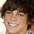 Pixelated close-up of a person with dark brown hair, light skin tone, and visible teeth in a smiling expression.
