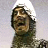 Pixelated static image of a person with dark hair and brown skin wearing a green garment, set against a light background with white highlights.