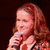 A person with long red hair holds a microphone while text reads "Singing is everything to me" on the right.