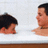Two pixelated human figures face each other against a light background with brown horizontal bands at top and bottom.