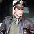 A pixelated figure in a military-style uniform with a peaked cap, standing against a dark background with light patches.
