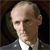Static pixelated image of a person in military uniform with visible insignia on shoulders, dark background, and light-colored shirt underneath.