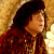 Static pixelated image of a person with long dark hair wearing a red garment against a warm-toned background.