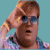 A 50x50 pixel animated buddy icon featuring a cartoon character with brown hair and blue eyes in two sequential frames showing hand-to-head motion against a teal background.