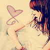 A pixelated image of a person with long brown hair wearing a white top, holding a heart-shaped object near their face.