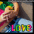Pixelated image of a person with light hair holding a yellow flower near their face, with colorful text reading "LOVE" at the bottom.