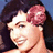 Pixelated close-up of a person with dark hair and a pink bow, smiling against a blue background.
