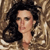 Pixelated image of a person with dark curly hair against a brown patterned background, wearing a light-colored garment with a textured pattern.