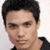 Pixelated close-up of a person with short dark hair wearing a dark shirt against a light background.