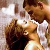 A close-up of a man and woman leaning toward each other with their eyes closed, set against a blurred background with light and dark tones.