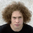 A pixelated image of a person with curly brown hair against a light background, with red text overlays on a black background.
