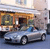 Pixelated image of a silver sedan with dark wheels parked in front of a building with orange and brown architectural details.