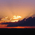Pixelated sunset scene with orange and yellow sky, dark landmass silhouette, and water reflection.