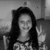 Black-and-white pixelated image of a person with long dark hair wearing a patterned top, seated against a blurred background.