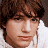 A pixelated image of a person with brown hair and light skin wearing a white top, next to green text reading 'OriginalIcons.com' on a dark background.