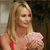 Pixelated image of a person with long blonde hair wearing a red strap top and holding a pink fluffy object against a blurred background.
