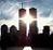 Pixelated static image of two tall buildings with a bright light beam between them against a cloudy sky background.