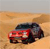A pixelated image of a dark-colored car with red accents on a sandy background, viewed from a low angle.