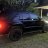 Pixelated static image shows a dark vehicle with blue and red lighting elements on a textured ground surface.